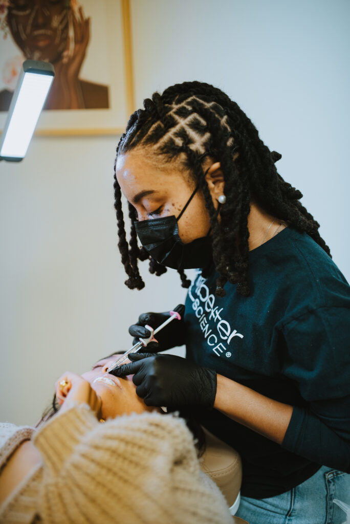 An experienced injector administers lip filler treatment to a patient. The injector carefully holds a syringe while delicately enhancing the patient's lips, providing a specialized cosmetic procedure for fuller and more defined lips.